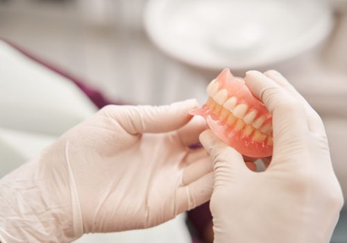 Cropped view of the dentist holding dentures in her hands. Dental prosthesis in the hands of the doctor close-up. Front view of complete denture. Dentistry conceptual photo. Prosthetic dentistry. False teeth
