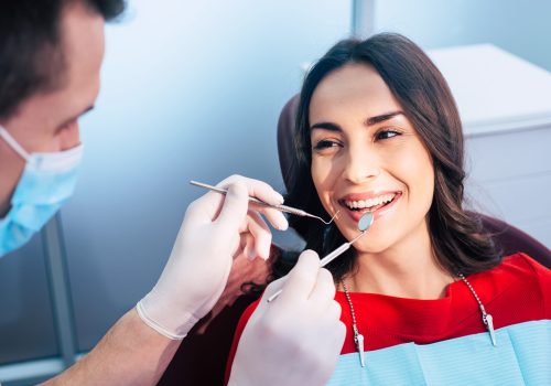 Wonderful treatment. Dentist in ear loop face mask and gloves is holding dental instruments and checking the result of his professional work in the dental center.